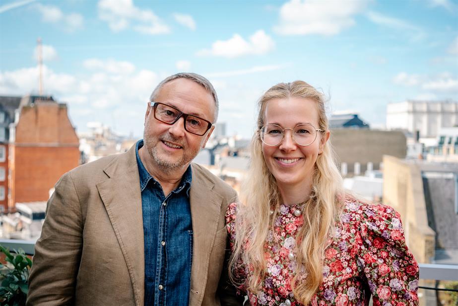 Andrew Hill and Chloe London smiling into the camera, against a London backdrop of blue sky with fluffy clouds 